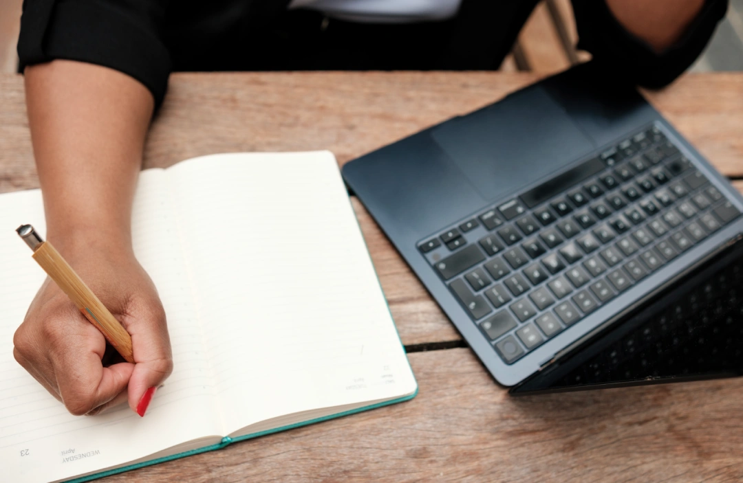 woman writes in planner with laptop nearby | Voyager Recovery Center